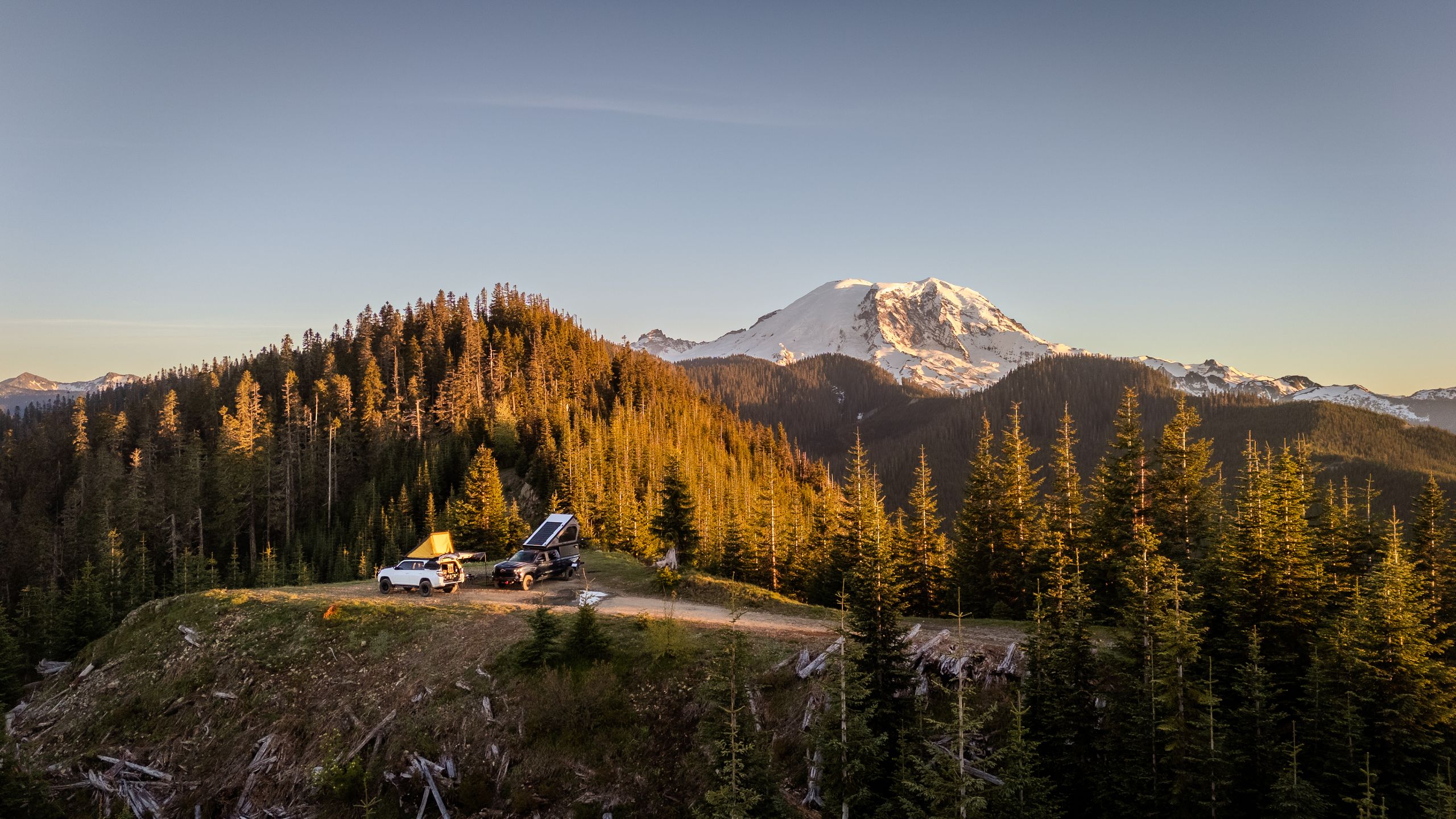 Overland vehicles and rooftop tents beneath a snow-covered mountain in the Pacific Northwest